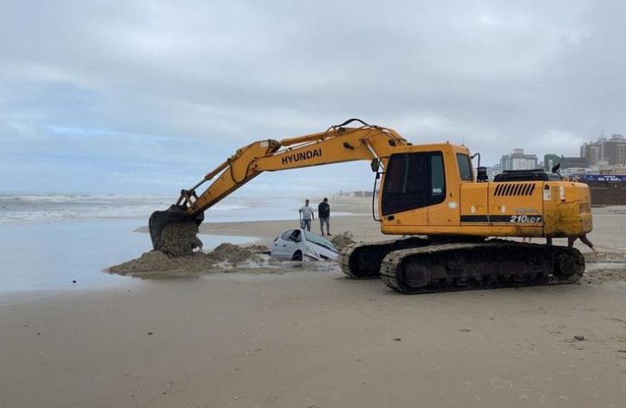 Mar agitado dificulta retirada de carro atolado na beira do mar, em Capão da Canoa